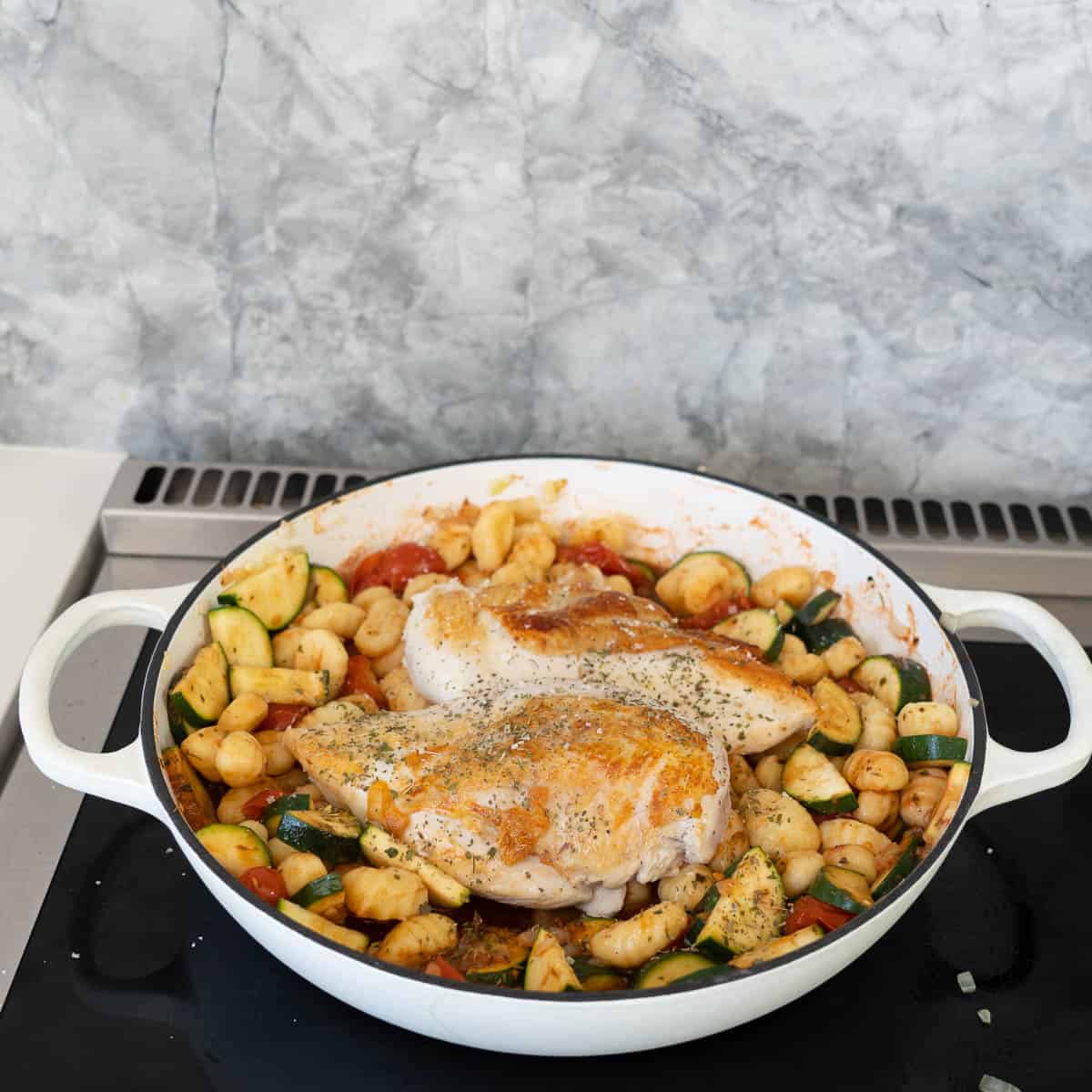 Two chicken breasts on a bed of gnocchi and vegetable tomato sauce ready to go in to the oven.
