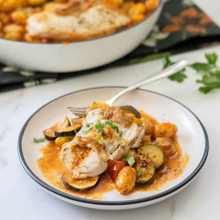 Slices of chicken sitting on a bed of gnocchi in a tomato based sauce, pieces of zucchini visible.