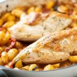 Two chicken berasts with crispy skin in a casserole dish with gnocchi and vegetables.