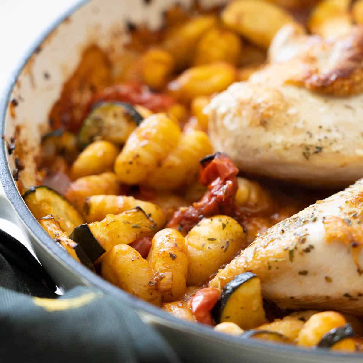 Cooked in a tomato and vegetable sauce in a white casserole dish.