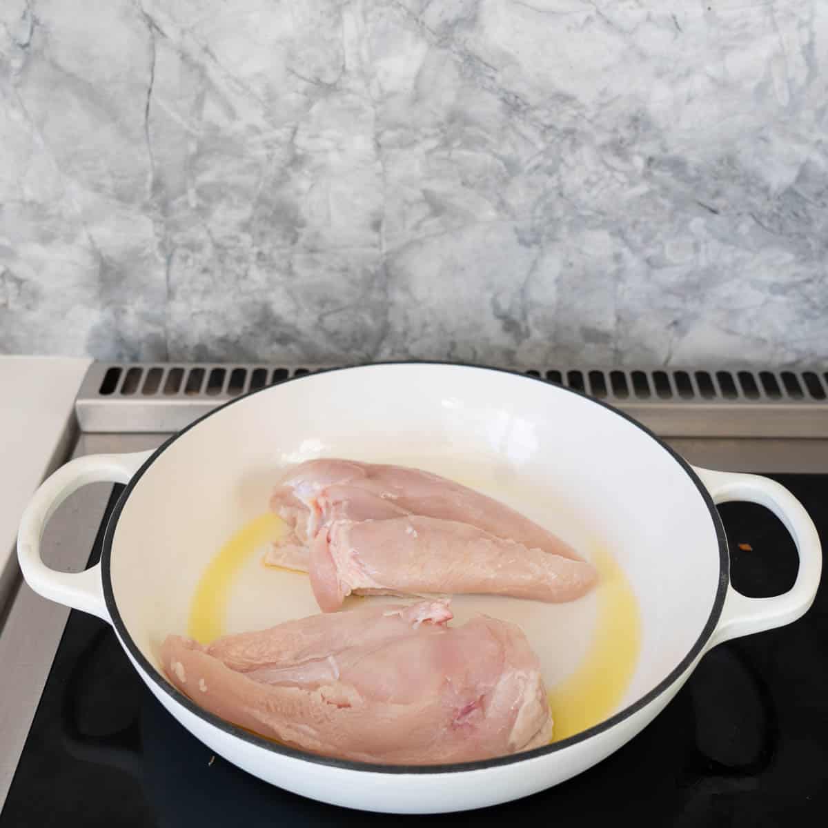 Two chicken breasts skin side down in a large white casserole dish.