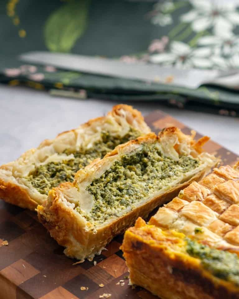 Two slices of pie on a wooden chopping board showing the green spinach and cheese filling.