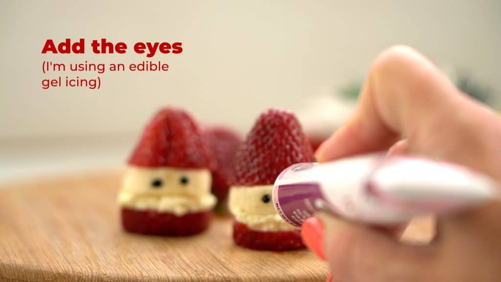 hand holding gel icing drawing eyes onto a strawberry Santa.