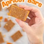 Womans hand holding a piece of apricot bar, baking paper on benchtop below with rest of apricot bars. Text overlay; 3 Ingredient Apricot Bars, no-bake recipe.