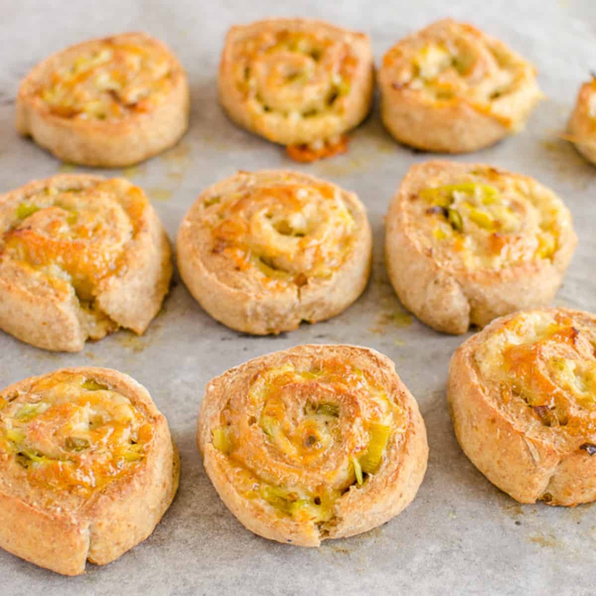 Wholemeal scrolls on a baking paper lined sheet. Cheese and leek filling visible.