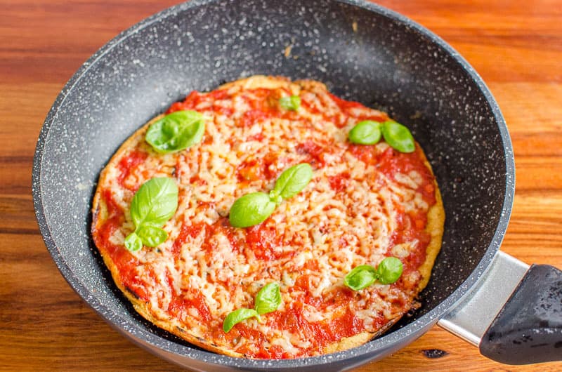 Pizza in a frying pan, topped with tomato sauce, melted cheese and basil leaves. 