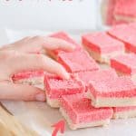 childs hand reaching for a slice of pink and white coconut ice