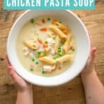 creamy chicken pasta soup in a white bowl on a wooden surface, childs hands reaching out to grab it