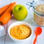 Small bowl of pureed carrot apple on benchtop, two carrots and a green apple next to the bowl.