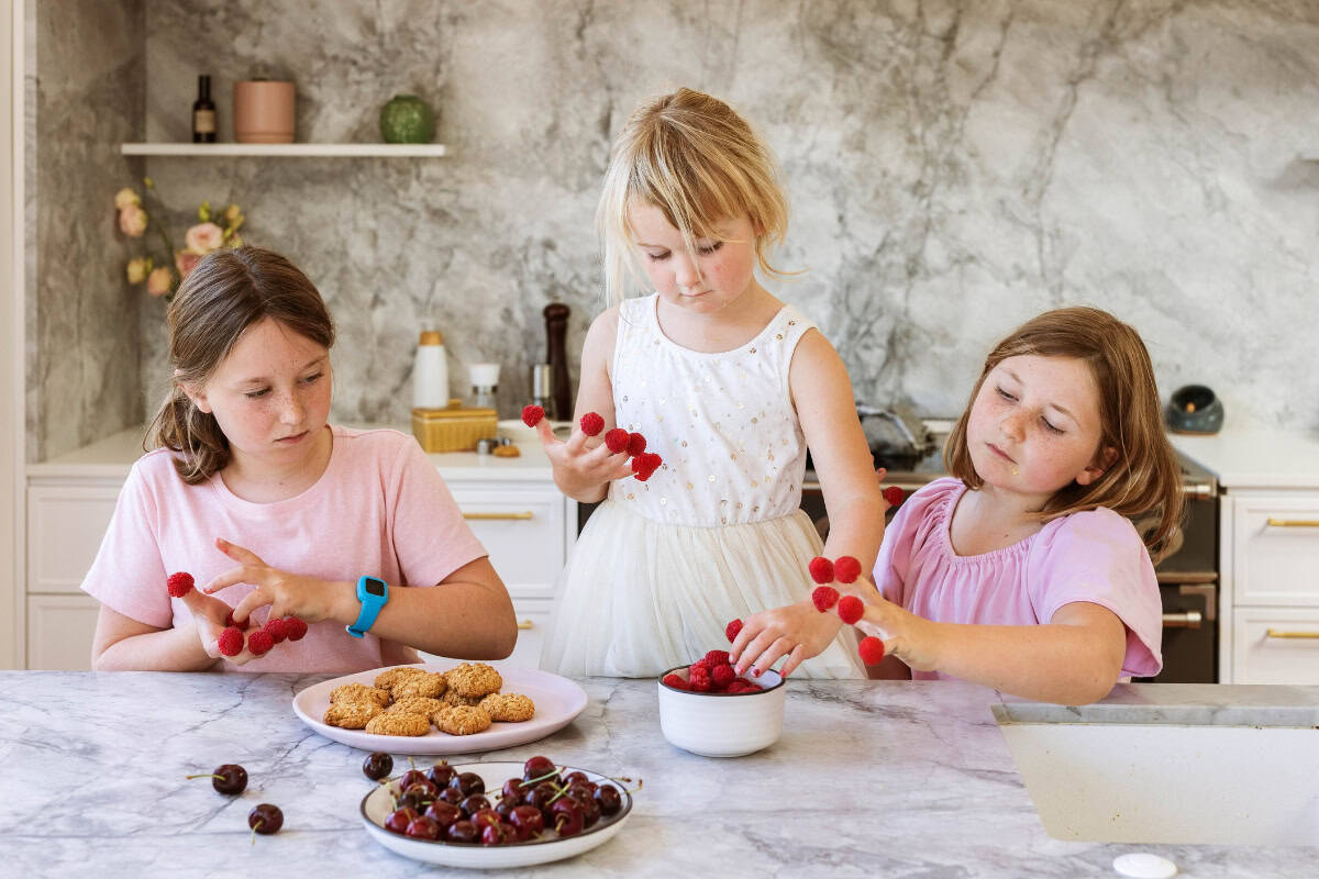 Three girls in a kitchen making cookies and eating raspberries.