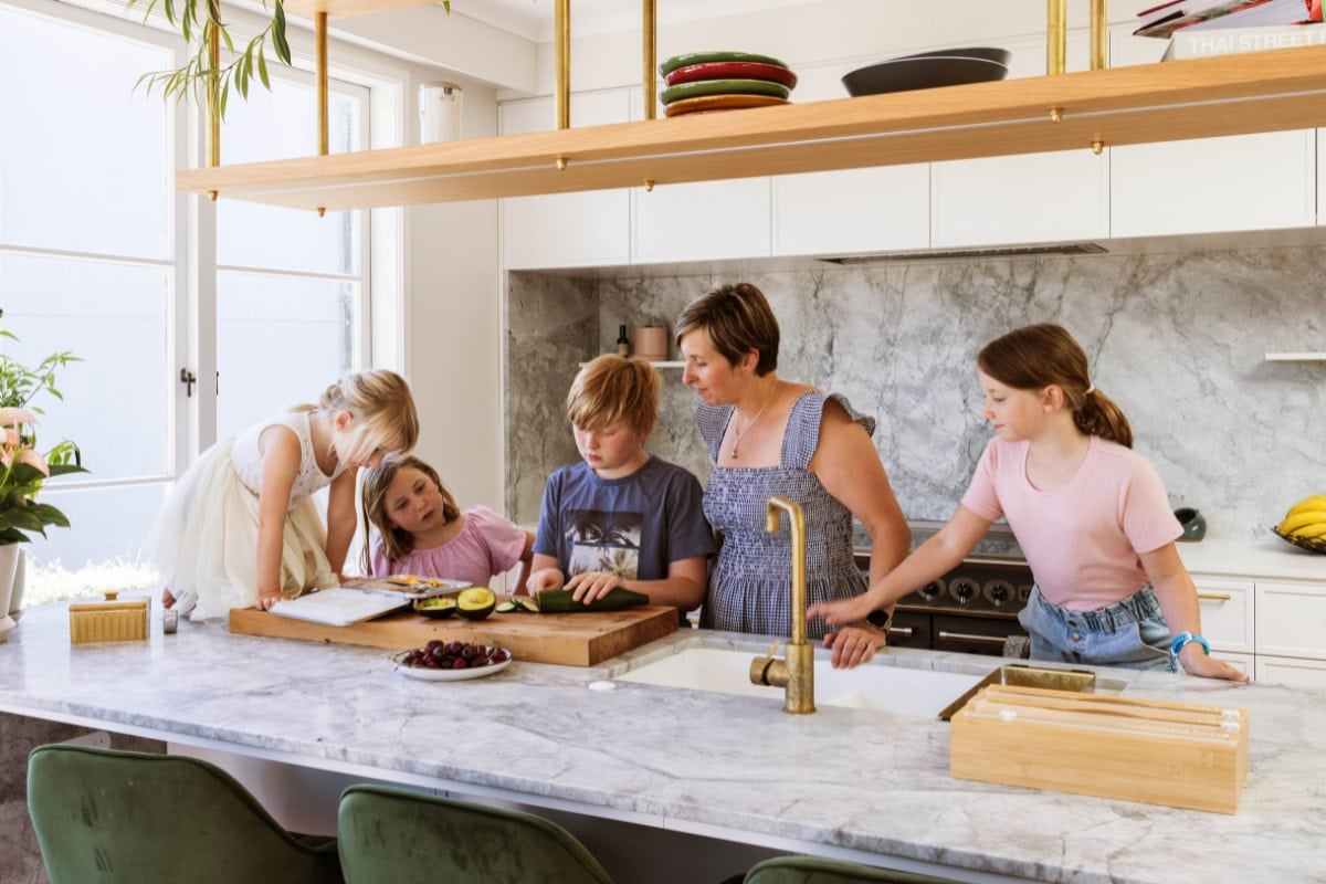 A mother with four young children cooking in a kitchen.