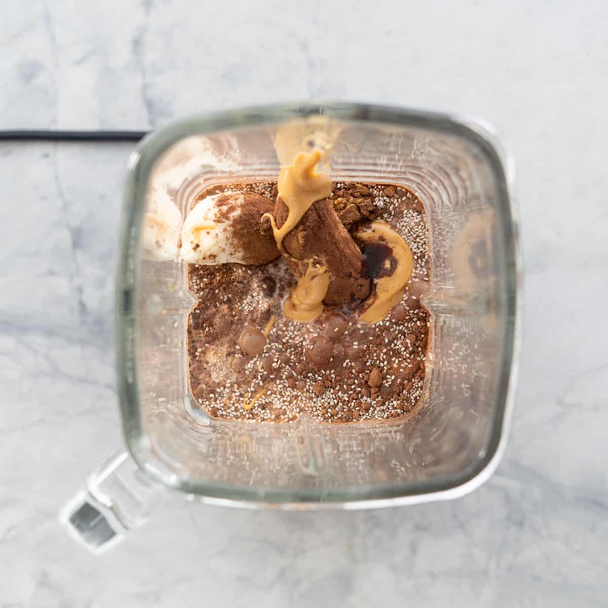 Looks down into the jug of a blender, milk, chia seeds, cocoa and peanut butter visible.