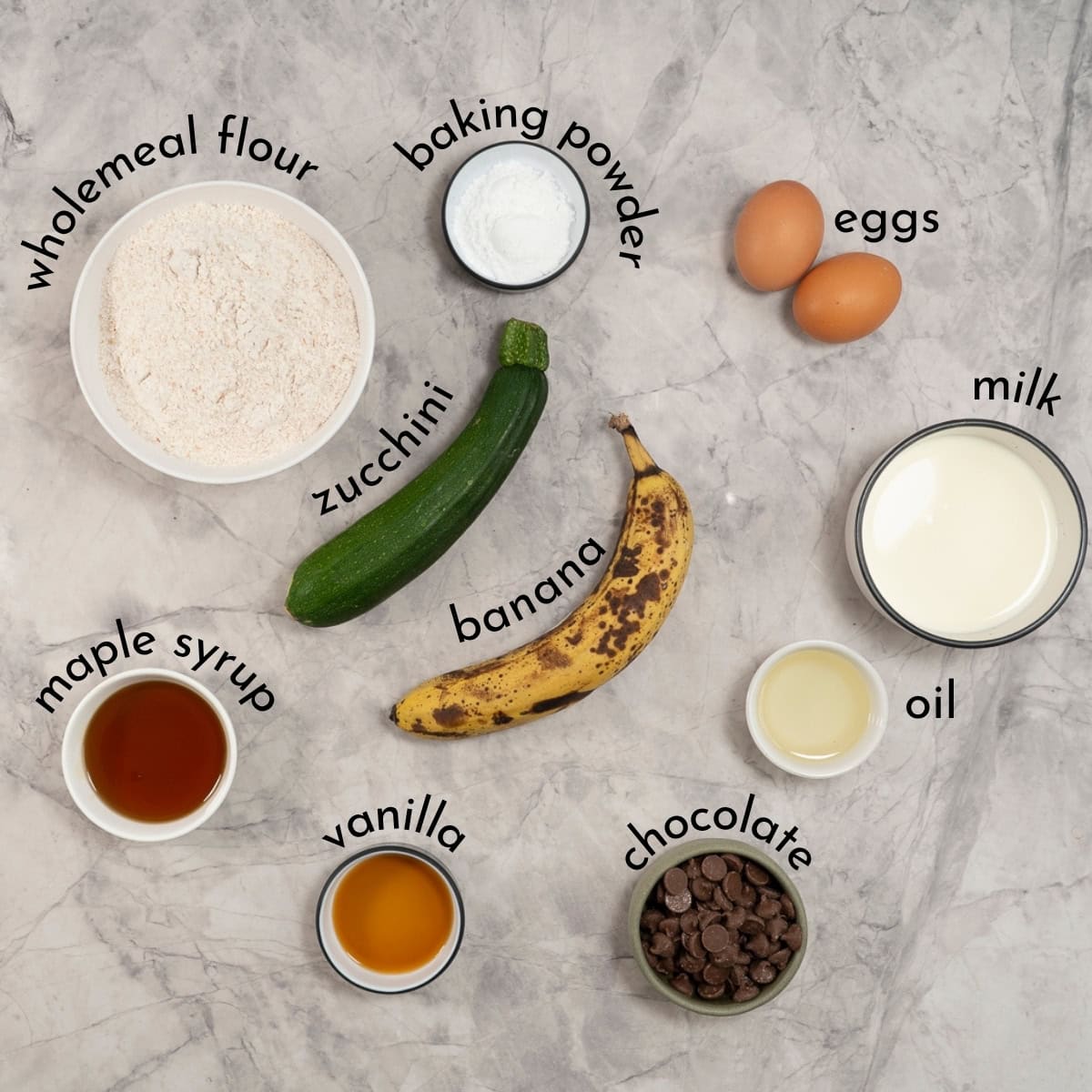Ingredients for Banana Zucchini Muffins on benchtop with text overlay.