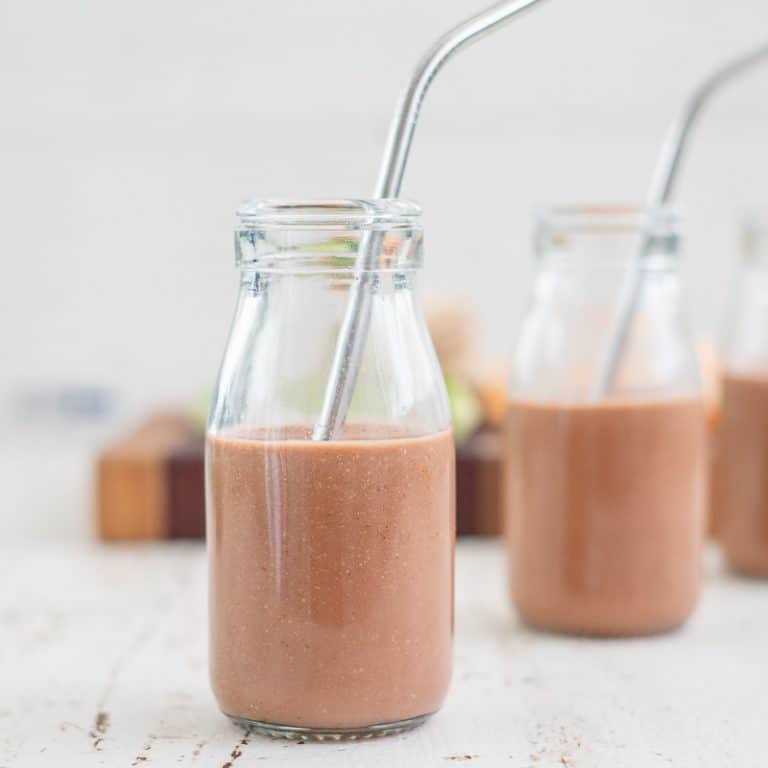 Two small glass jug bottles with chocolate milk inside with metal straws inside.