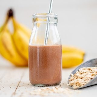 A small glass bottle of chocolate milk in front of bananas and a rolled oats.