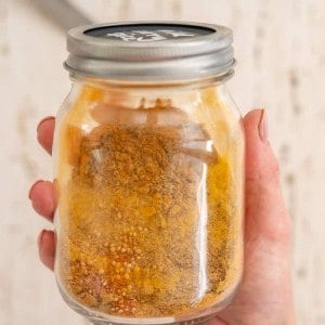 Hand holding a jar with curry spices inside.
