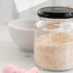 spoonful of cooked baby porridge on a pink baby spoon with a jar of baby oats in the background