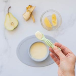 A spoonful of baby custard being held up above a bowl of custard.