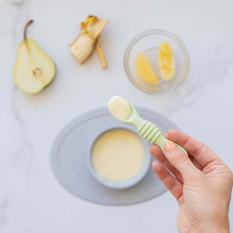 A spoonful of baby custard being held up above a bowl of custard.