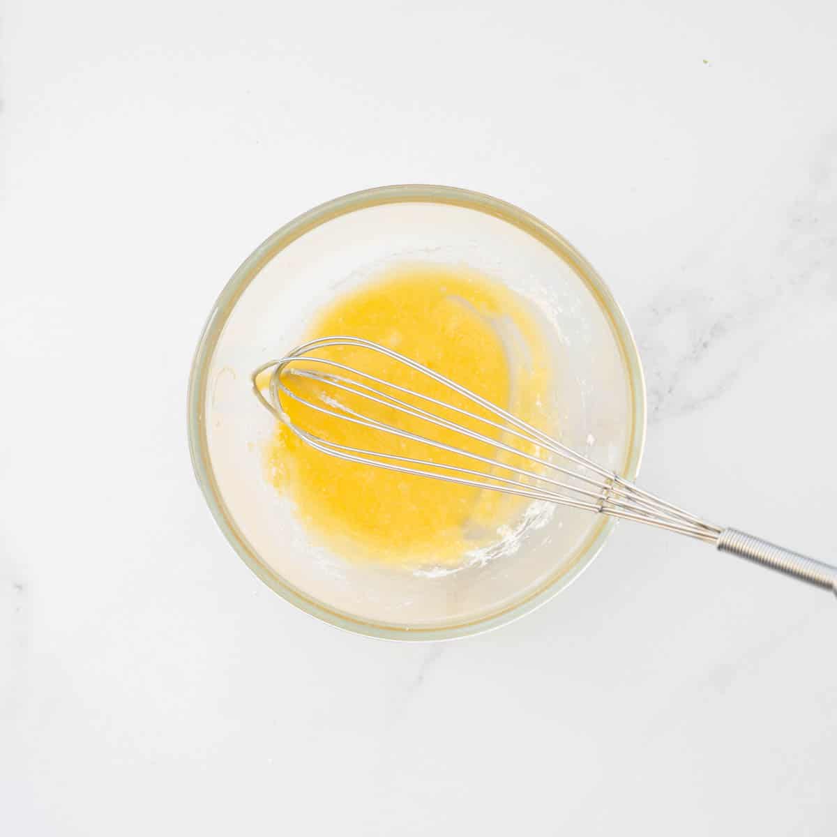A yellow paste of cornflour and egg yolk in a small bowl with a whisk resting to the side.