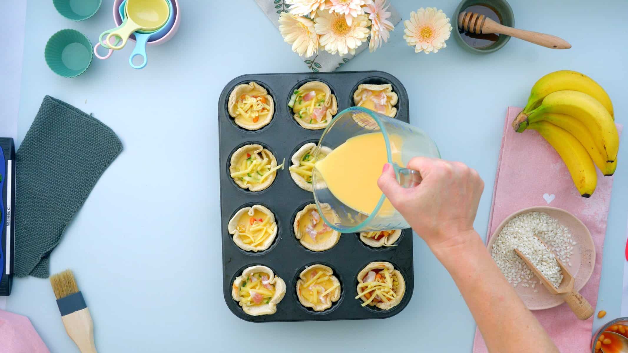 A jug of whisked egg being poured into bread cases.