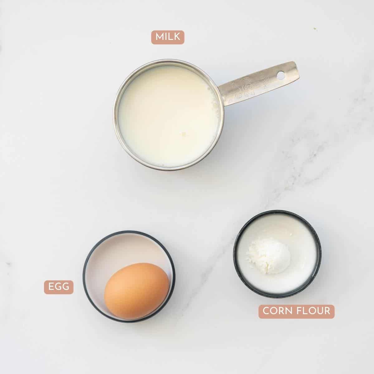 The ingredients to make custard laid out on a bench top with text overlay.