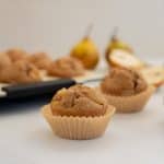 pear muffin in a muffin case on a marble bench top with a sliced pear in the background
