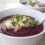 White bowl with beet soup inside topped with garnish.