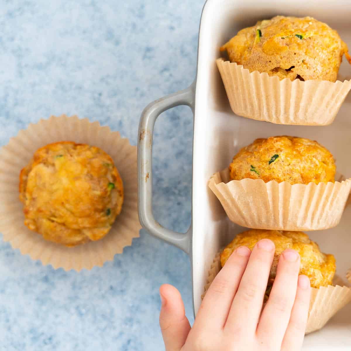 A child's hand reaching for 1 of 4 vegetable muffins in muffin cases