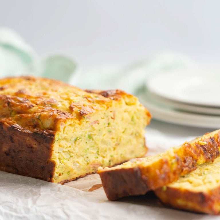 close up shot of zucchini slice sitting on a chopping board, plates and tea towel in the background