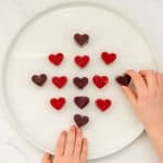 fruit gummies on a white plate with 2 children's hands reaching for them