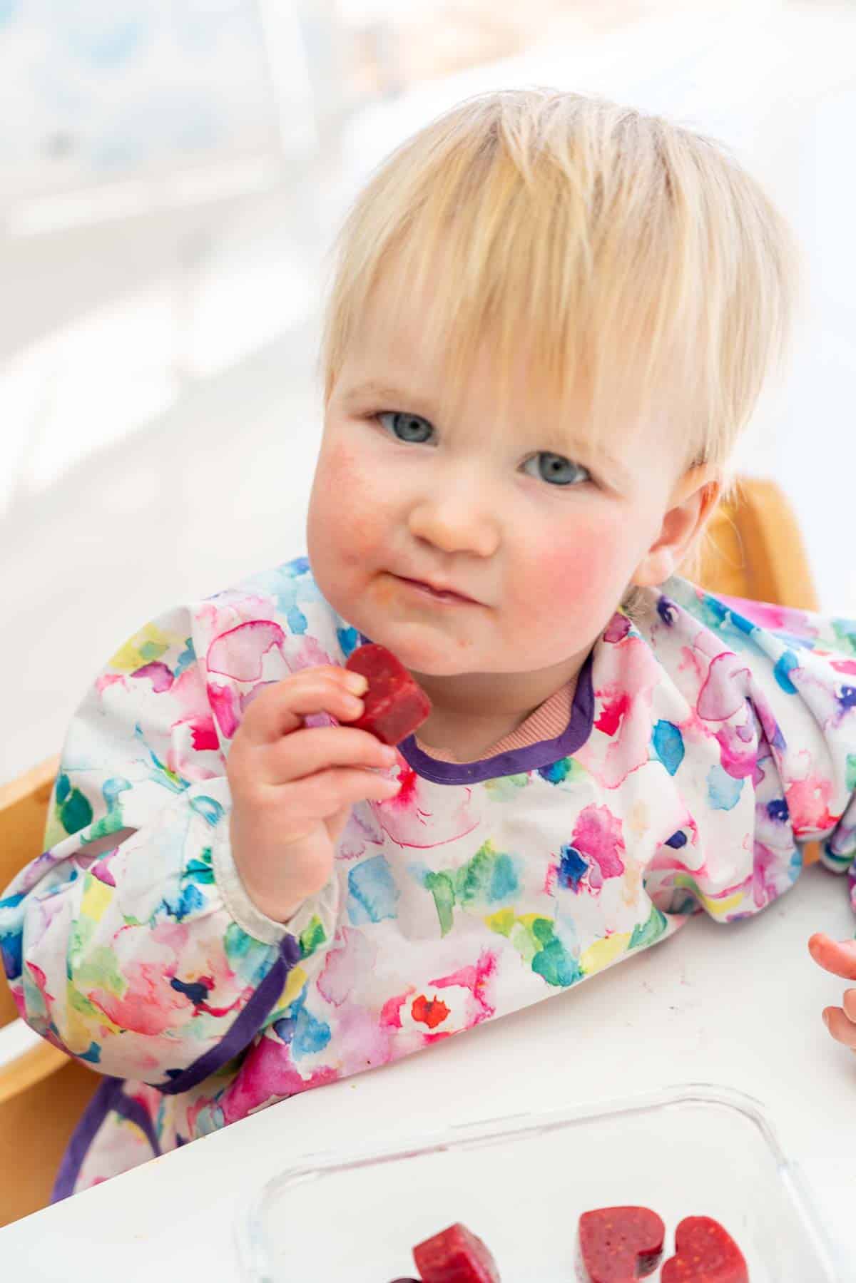 toddler in a colourful bib eating a fruit gummy