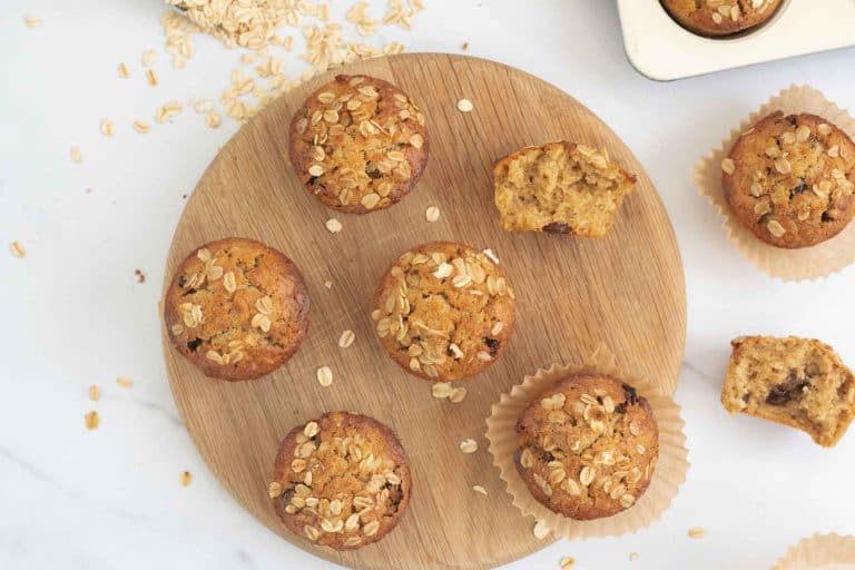top down shot of oatmeal muffins on a round wooden tray with a scoop of rolled oats