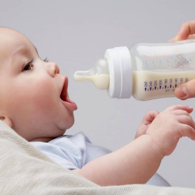baby with mouth open being offered a baby bottle