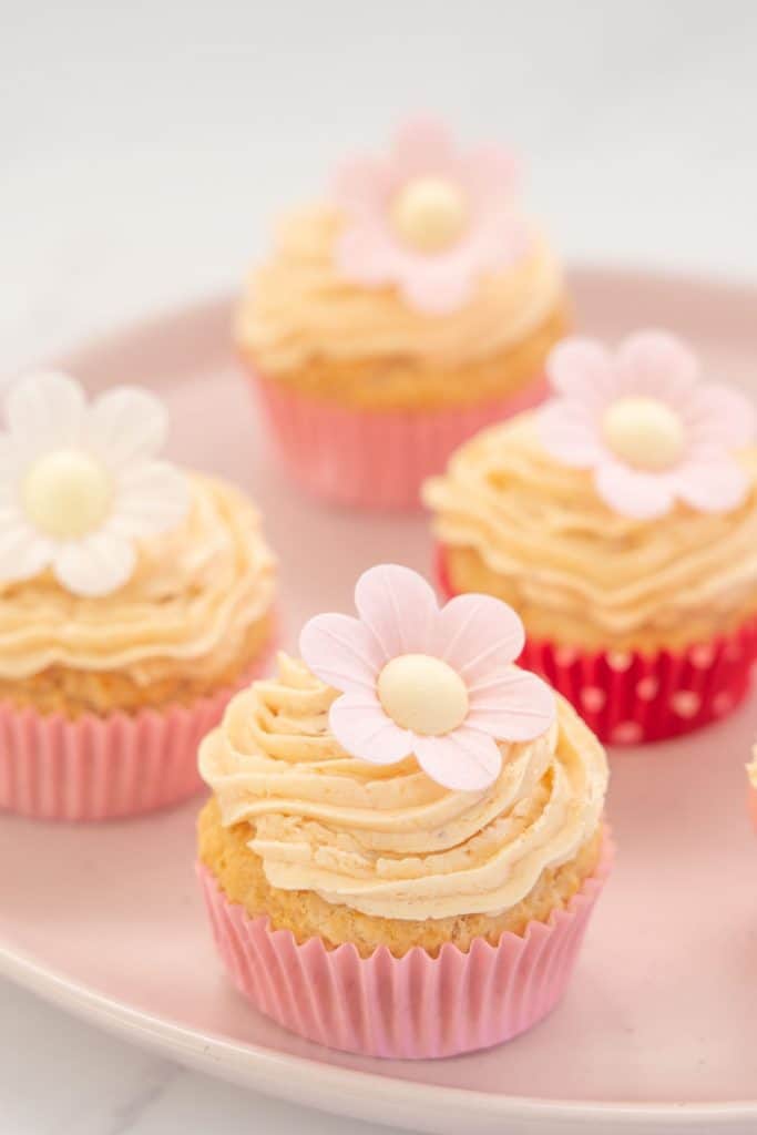 dairy free cupcakes topped with vegan butter cream and a flower sitting on a pink plate