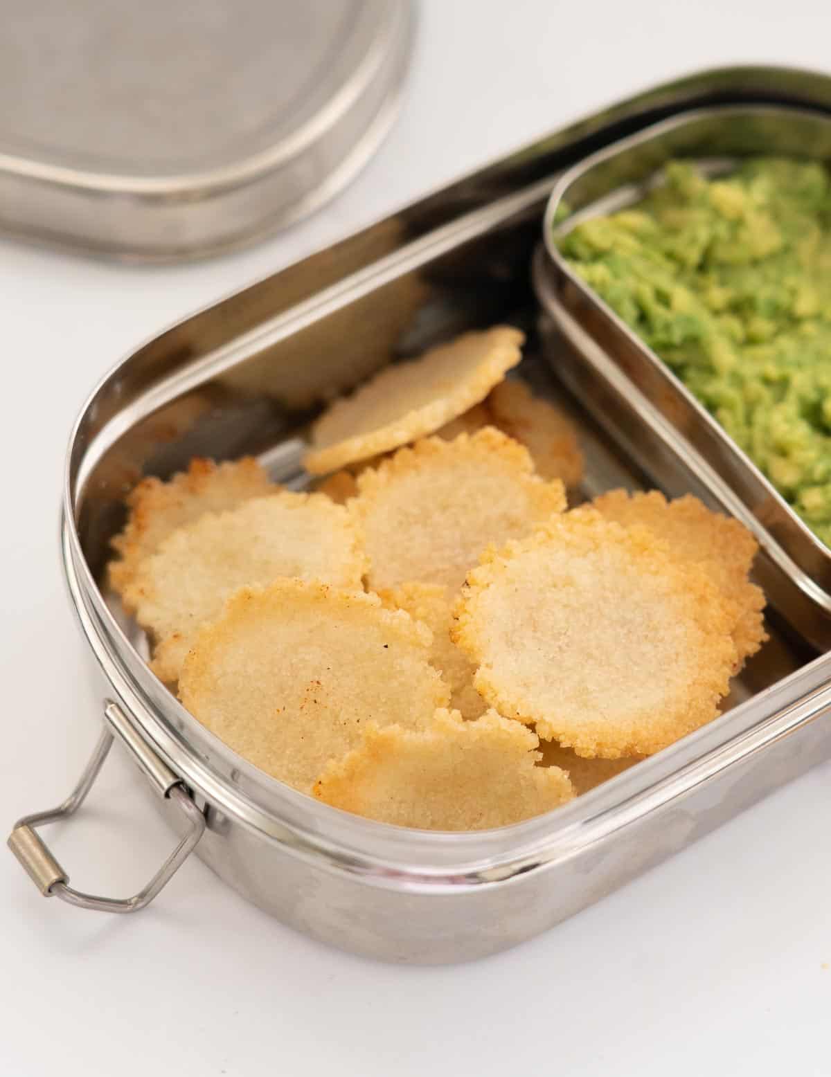Rice crackers in a divided stainless steal lunch box with mashed avocado