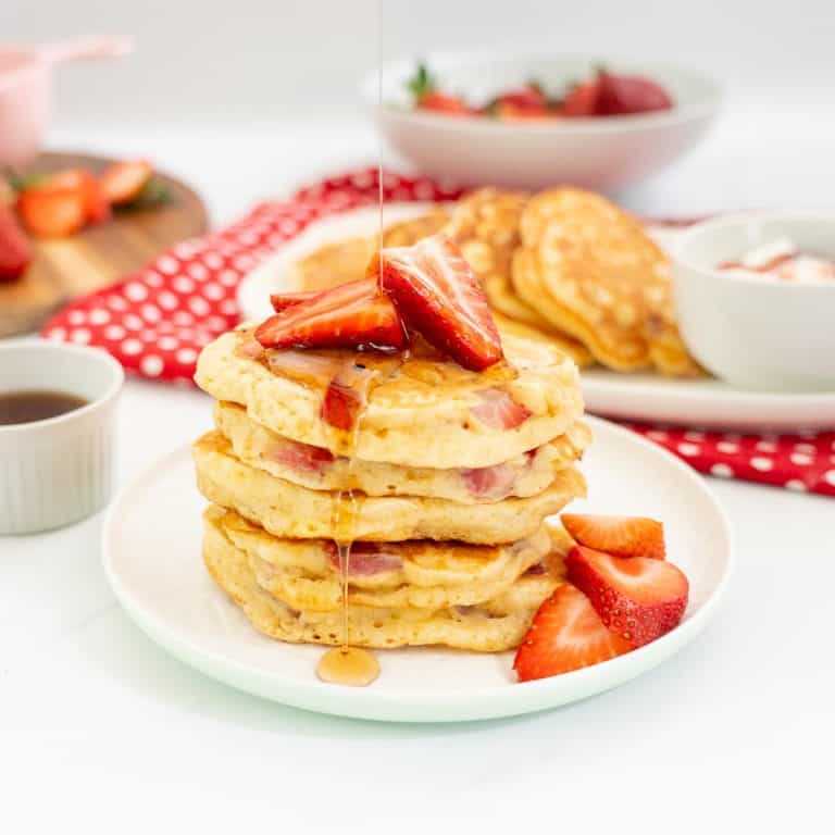 Stack of strawberry pancakes drizzled with maple syrup