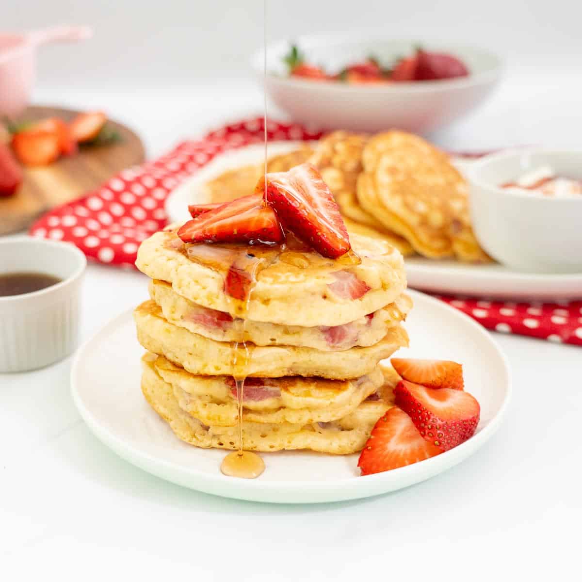 A stack of 5 strawberry pancakes drizzled with maple syrup