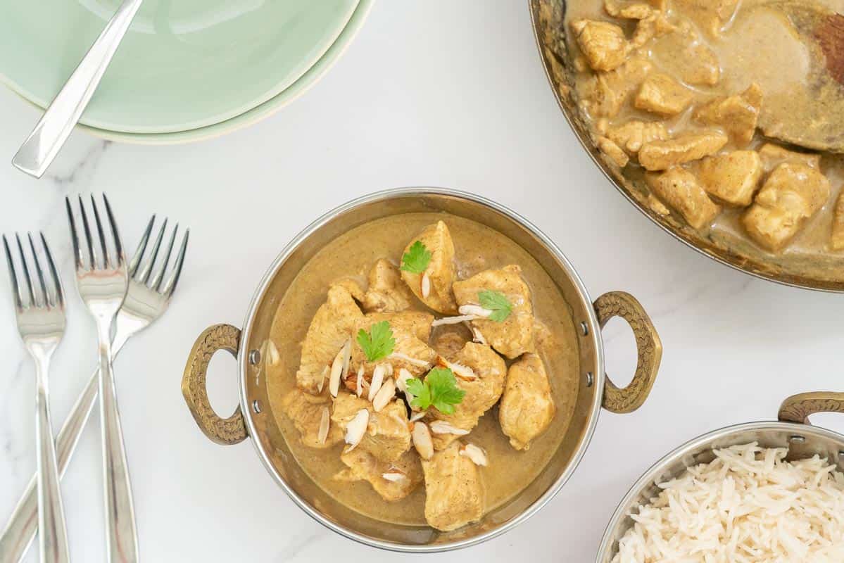 chicken korma in a copper bowl garnished with almonds and coriander leaves.