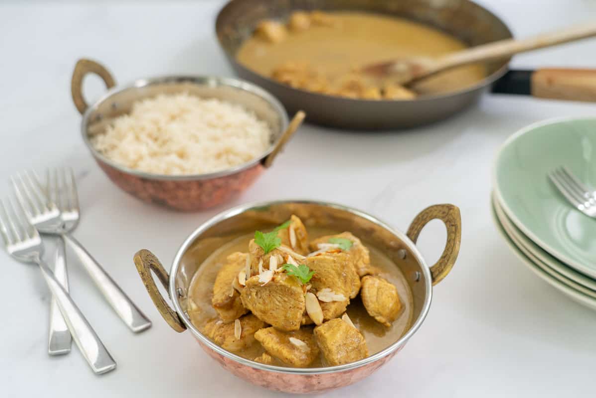 A bowl of chicken korma with rice in the background