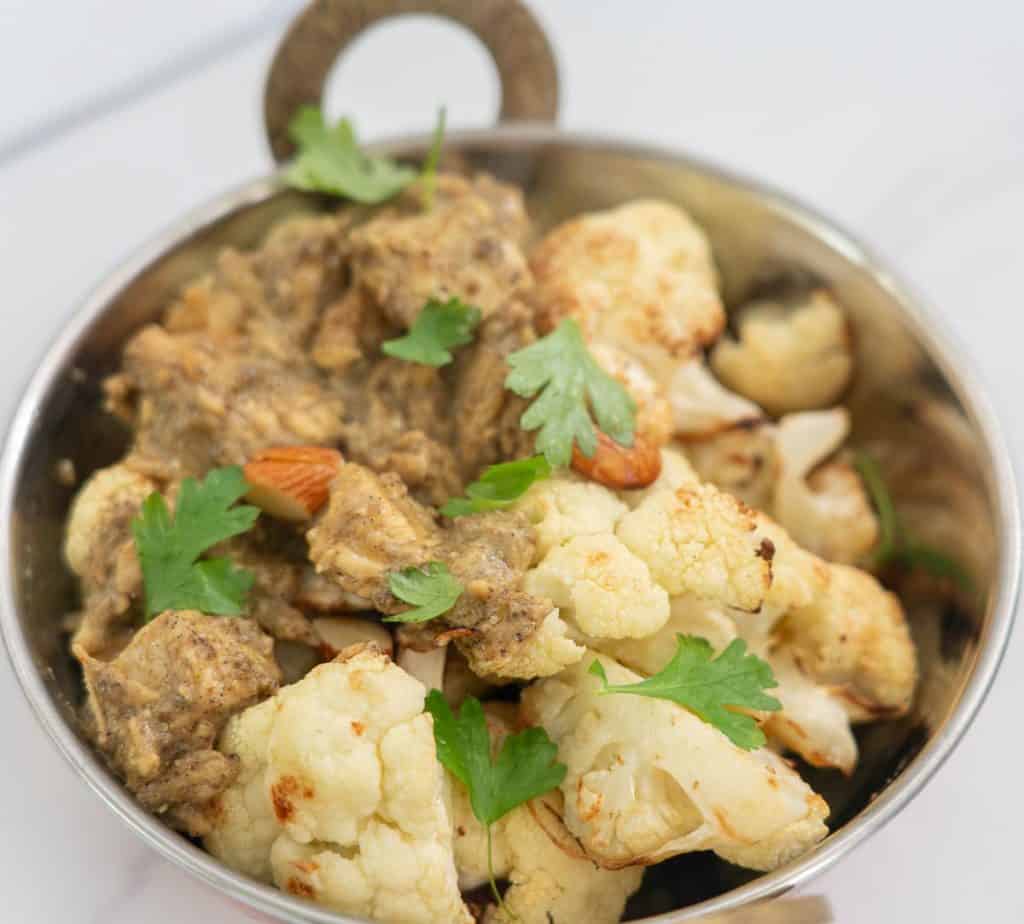 A bowl of chicken korma and roasted cauliflower and almonds garnished with coriander leaves