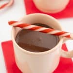 A pink mug filled with peppermint hot chocolate, decorated with candy canes