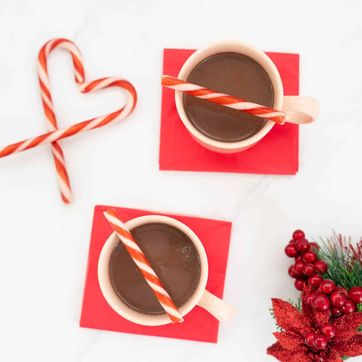 Top down view of 2 mugs of hot chocolate on red napkins, decorated with candy canes.