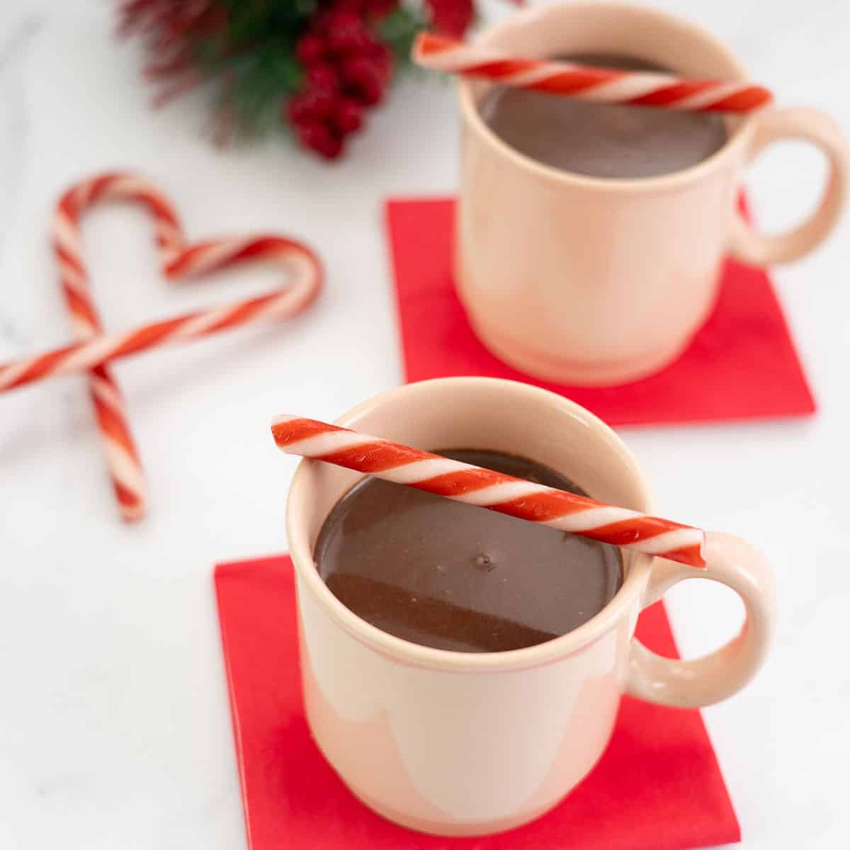Two peppermint hot chocolates in pale pink mugs decorated with red and white candy canes