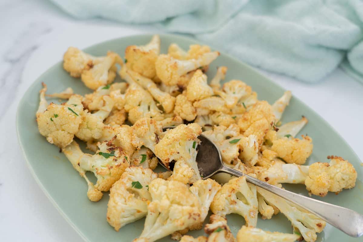roasted cauliflower on a green serving plate with a tarnished serving spoon