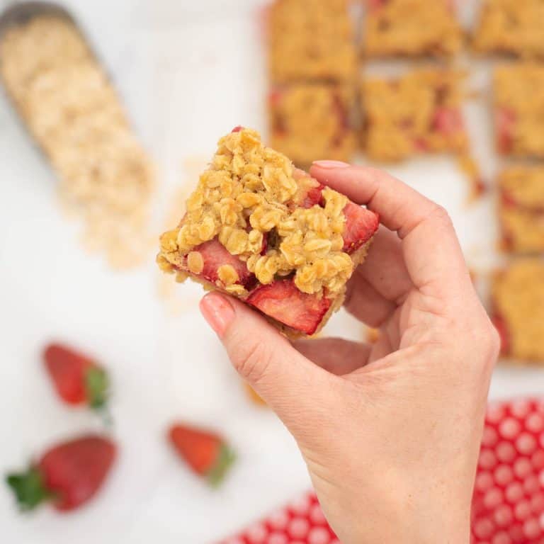 female hand holding a an oat bar with strawberries visible