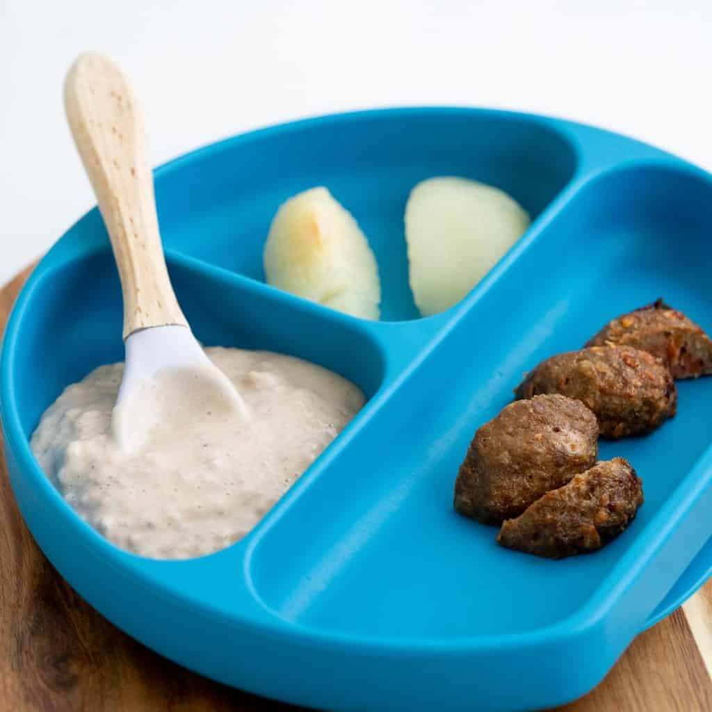 A blue divided baby plate containing chia pudding, pears and meat balls