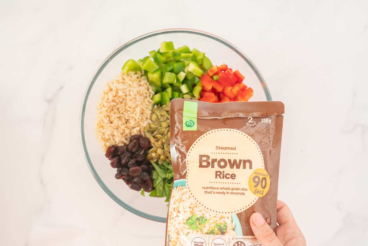 Woman's hand holding a pre-cooked brown rice package above a bowl of salad.