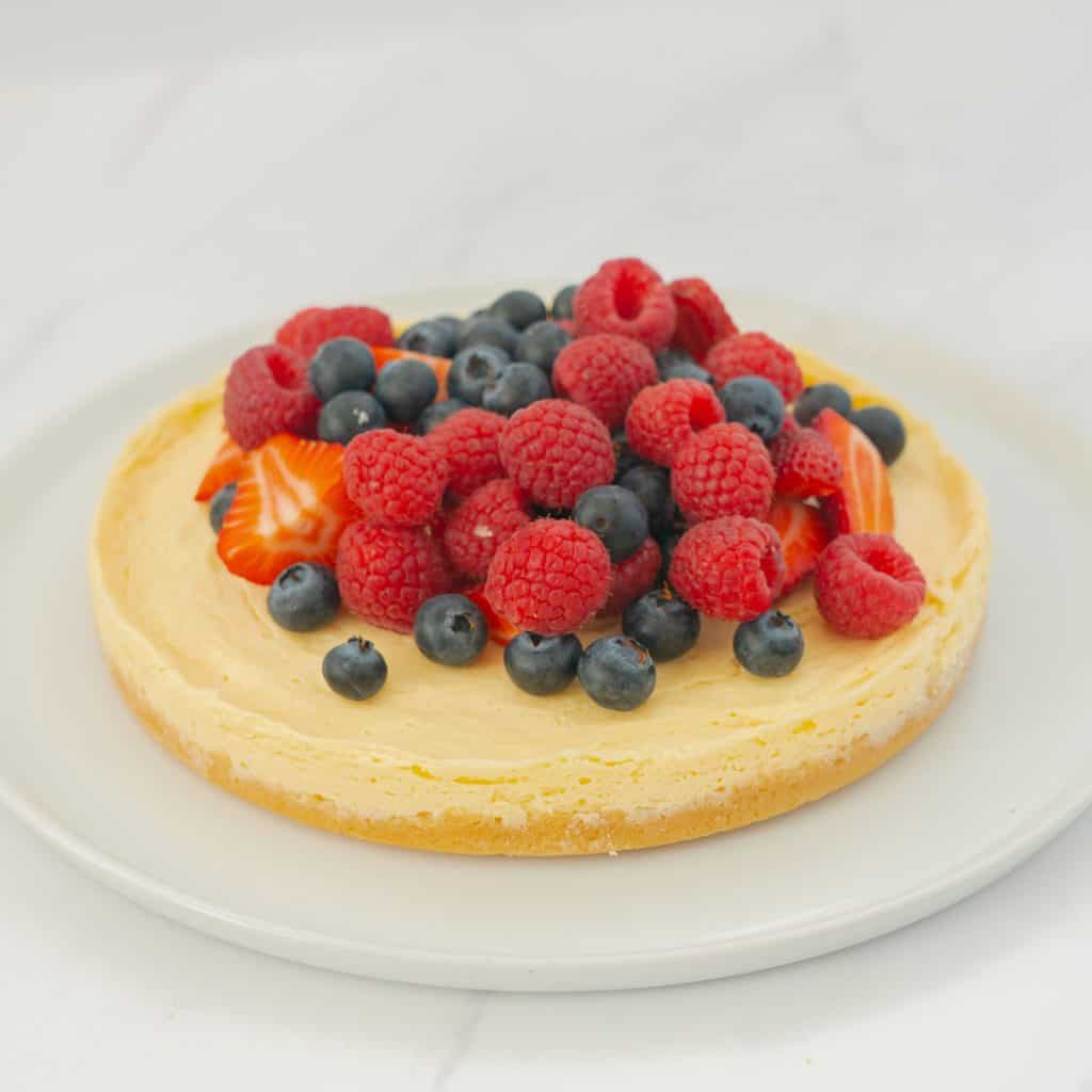 A round cheesecake with biscuit base topped with berries on a large white serving platter.