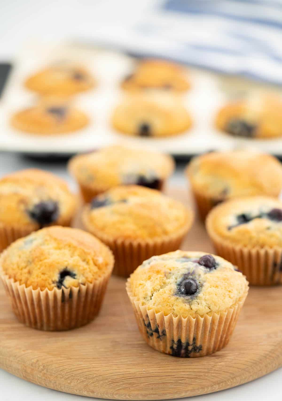 Blueberry studded muffins sitting on a circular wooden board.